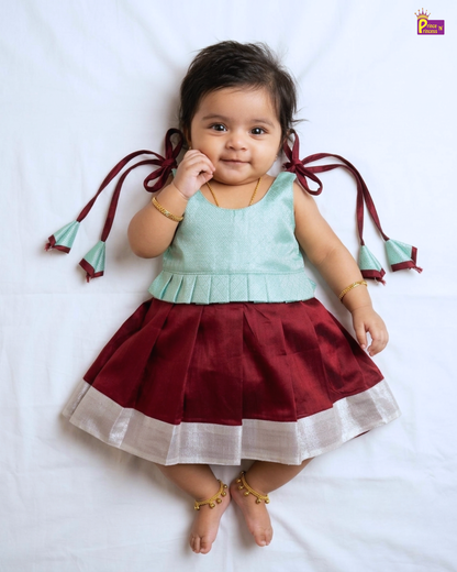 Baby wearing a light green top and red skirt with white trim on a white background