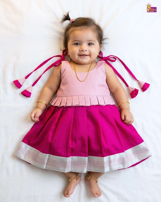 Baby wearing a pink and magenta dress with tassels on a white background