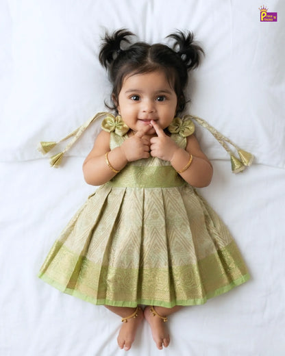 Baby in a green dress lying on a white surface