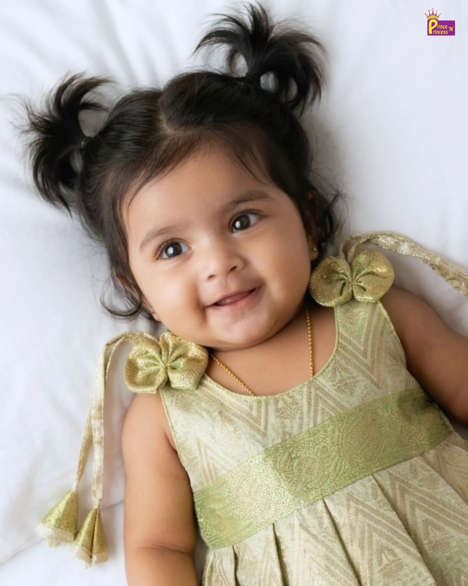 Baby in a green dress with bow details lying on a white surface