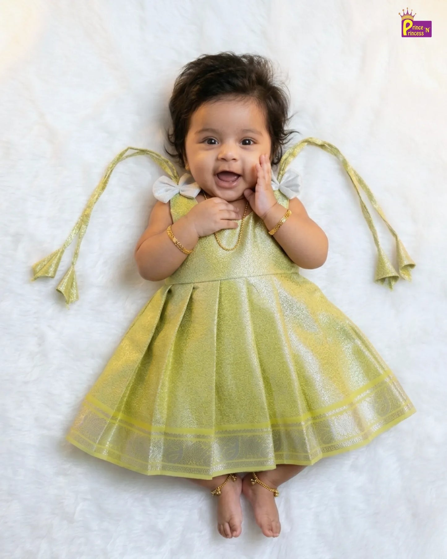 Baby in a yellow dress lying on a white surface