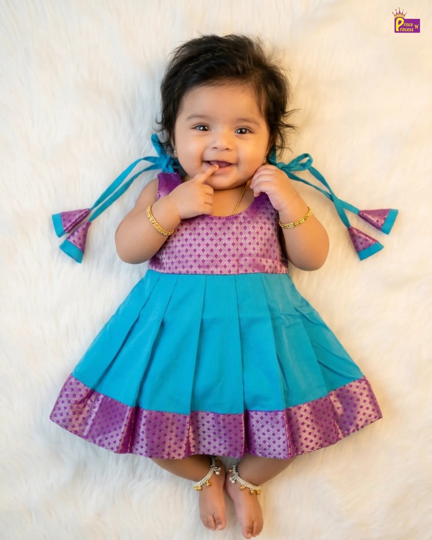 Baby wearing a blue and purple dress with tassels on a white background
