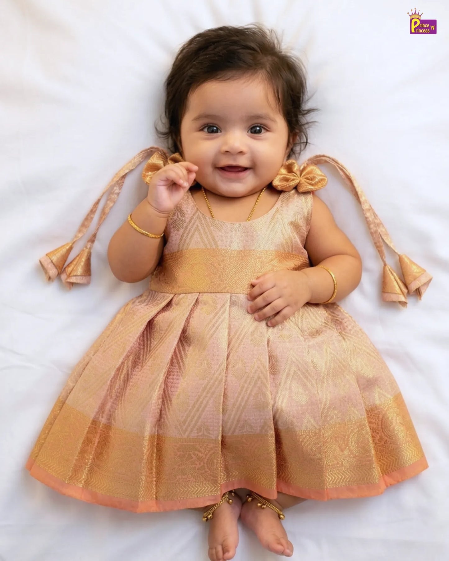 Baby wearing a gold dress with decorative elements on a white background