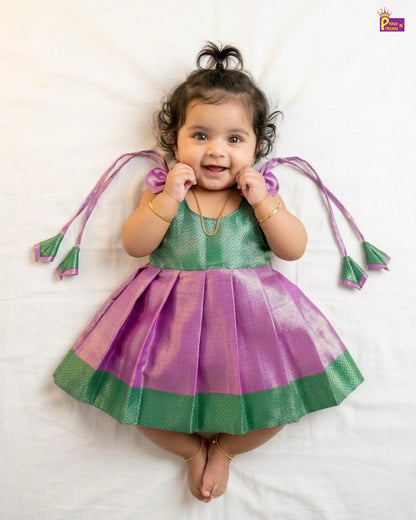 Baby wearing a green and purple dress with tassels on a white background