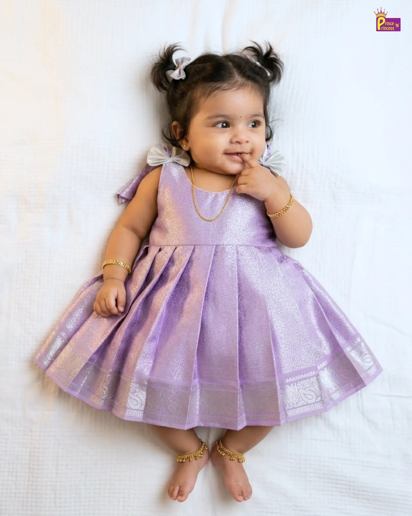 Baby in a purple dress lying on a white surface