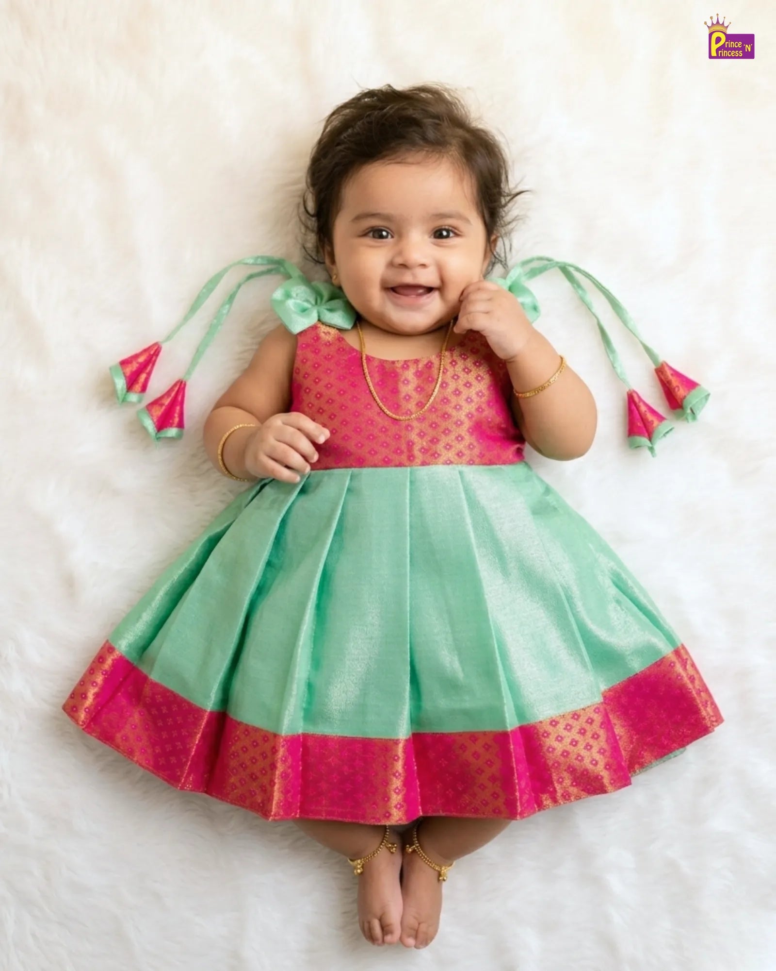Baby wearing a pink and green traditional outfit on a white background