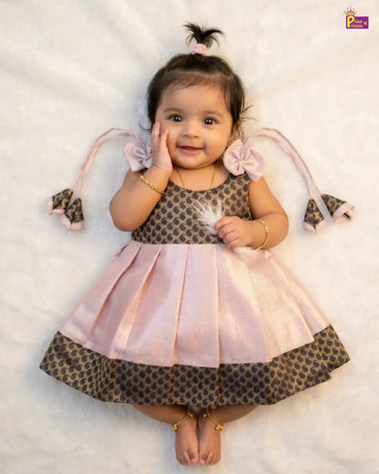 Baby wearing a pink and patterned dress with decorative ribbons on a light background