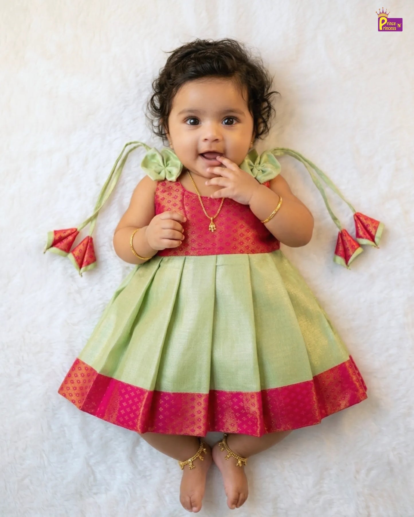 Baby wearing a colorful traditional outfit with a pink and green dress on a white background