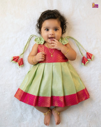 Baby wearing a colorful traditional outfit with a pink and green dress on a white background
