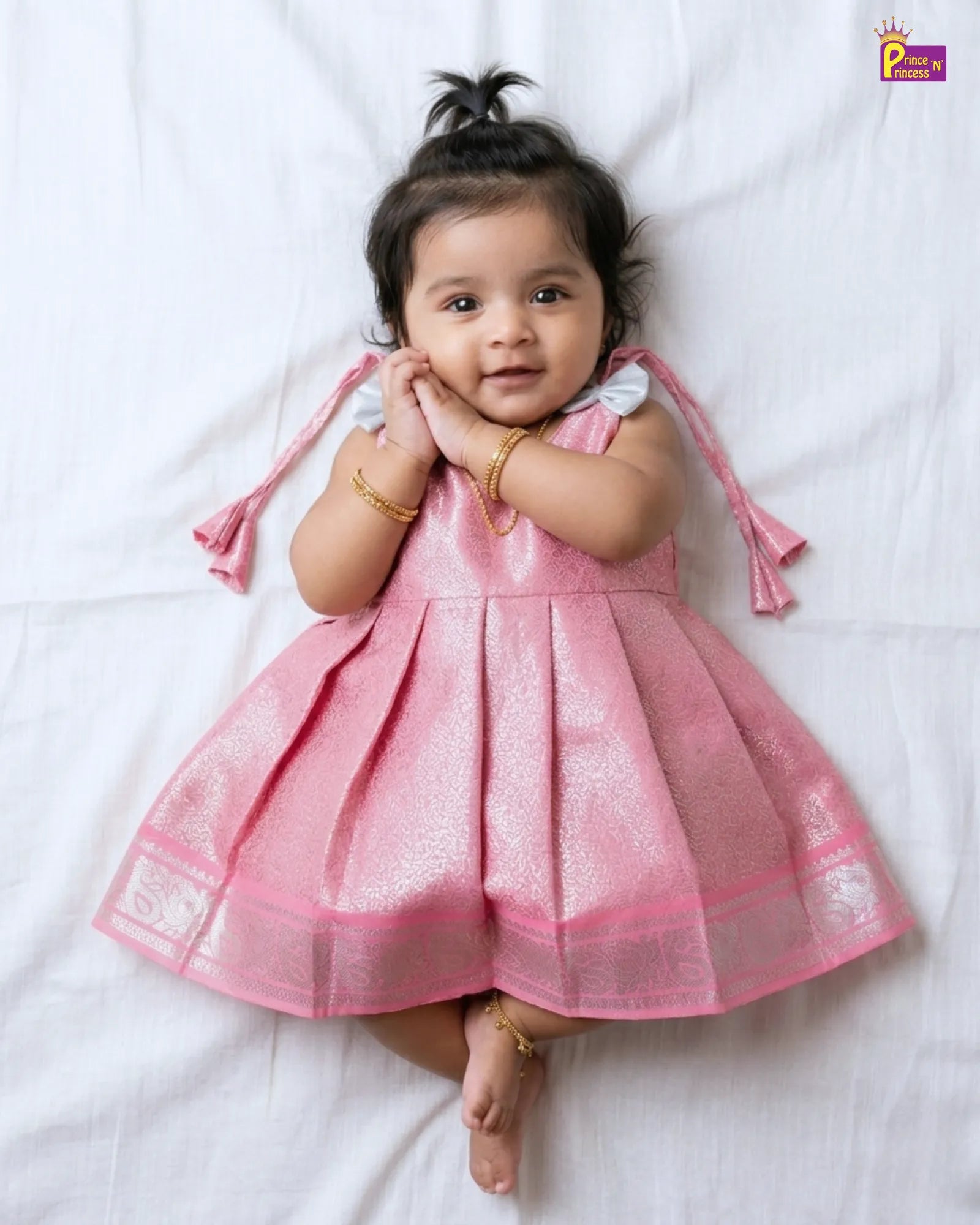 Baby in a pink dress lying on a white surface