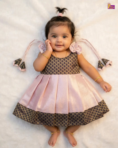 Baby wearing a pink and brown dress with decorative elements on a white background