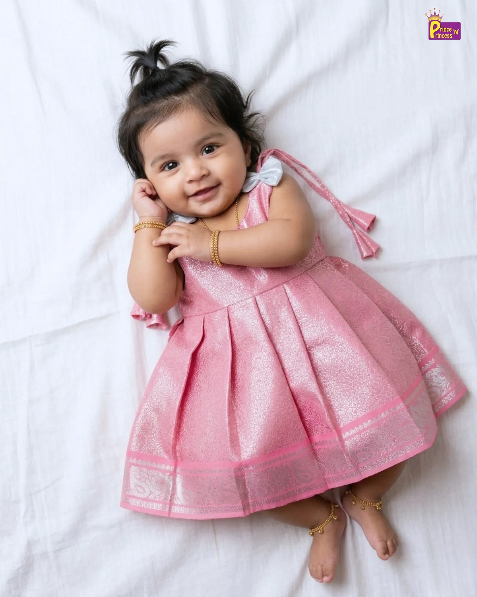 Baby in a pink dress lying on a white surface