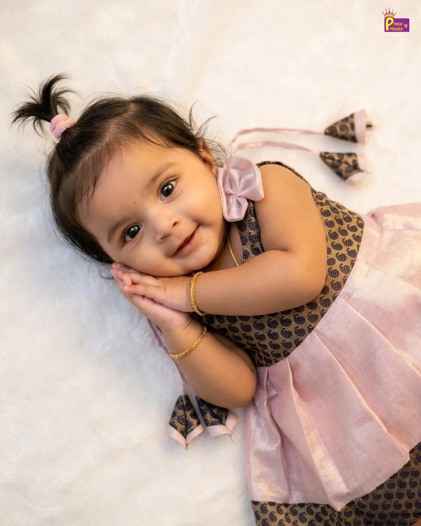 Child wearing a patterned dress with a pink bow and skirt, lying on a white surface.