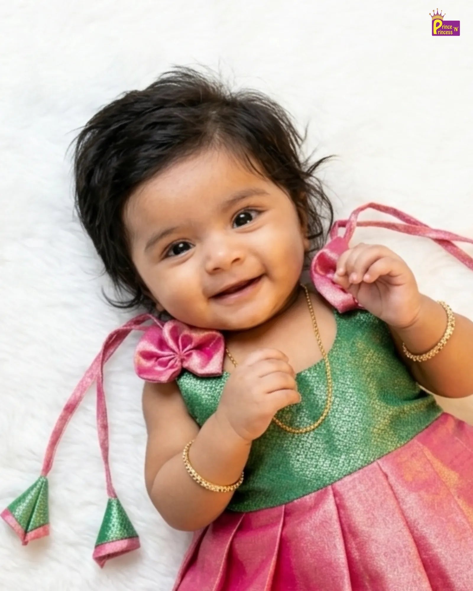 Baby in a green and pink traditional outfit with decorative elements on a white background