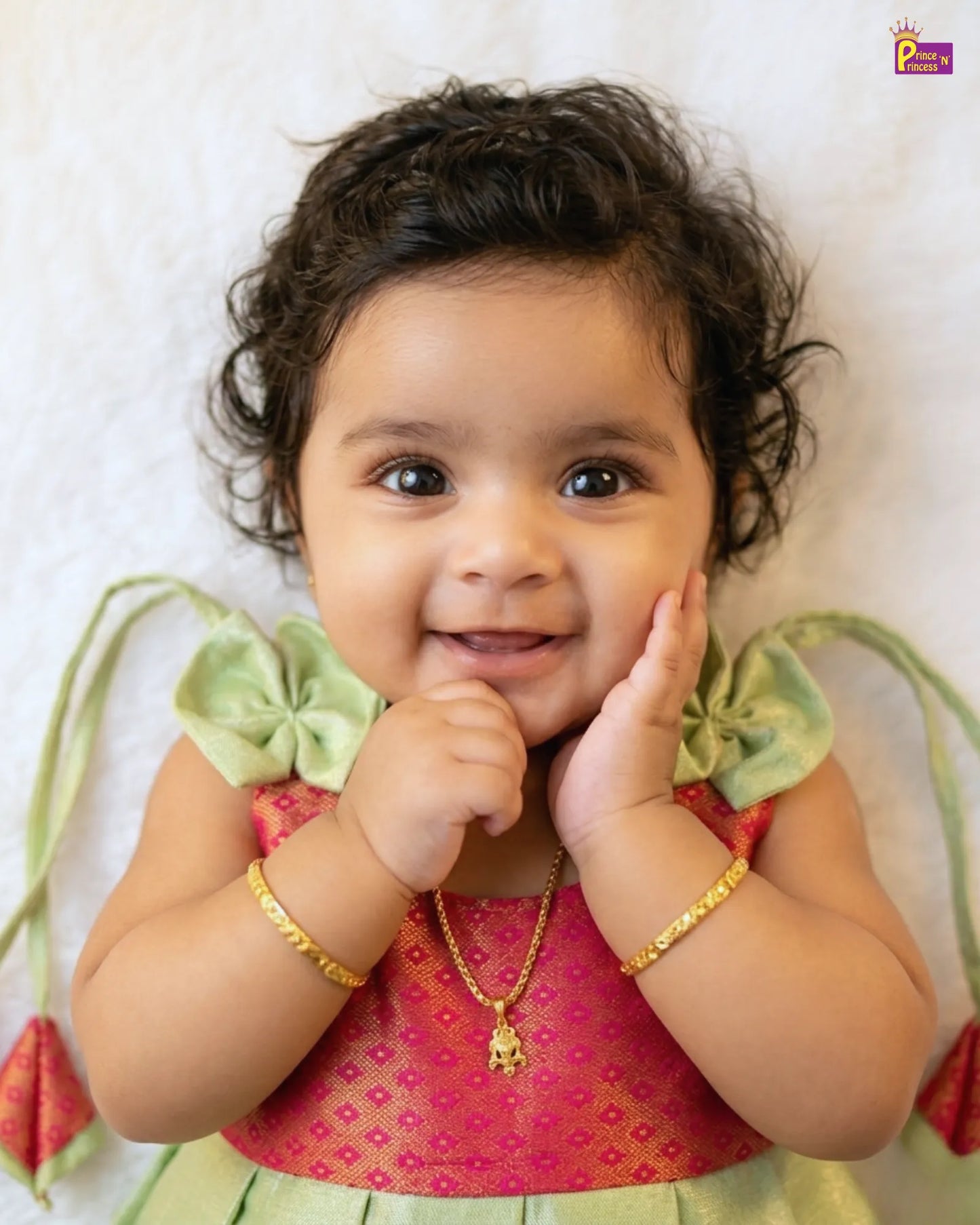 Baby wearing a pink and green outfit with gold jewelry on a white background