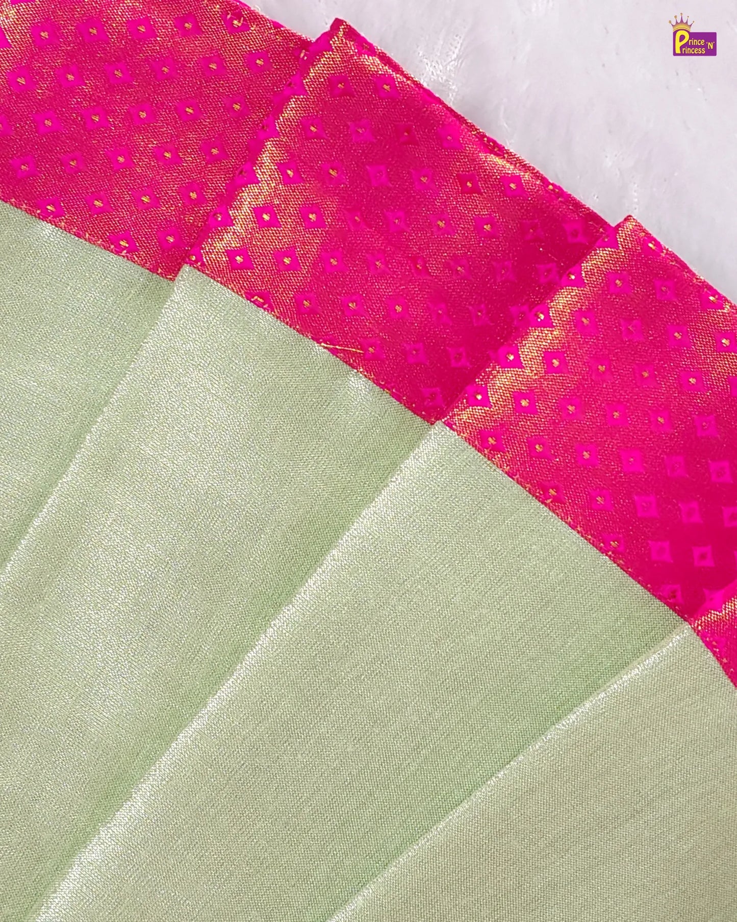 Close-up of a green fabric with pink border featuring diamond patterns.