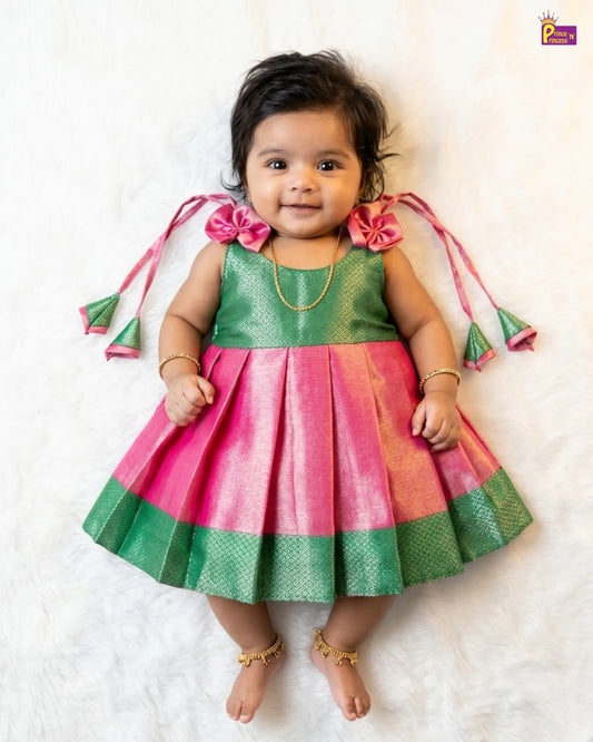 Baby wearing a green and pink traditional outfit with ruffles on a white background