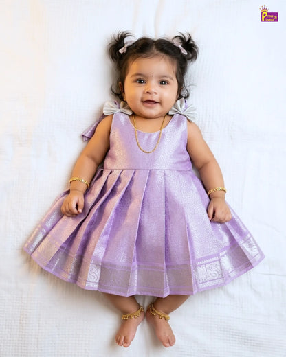 Baby in a purple dress lying on a white surface