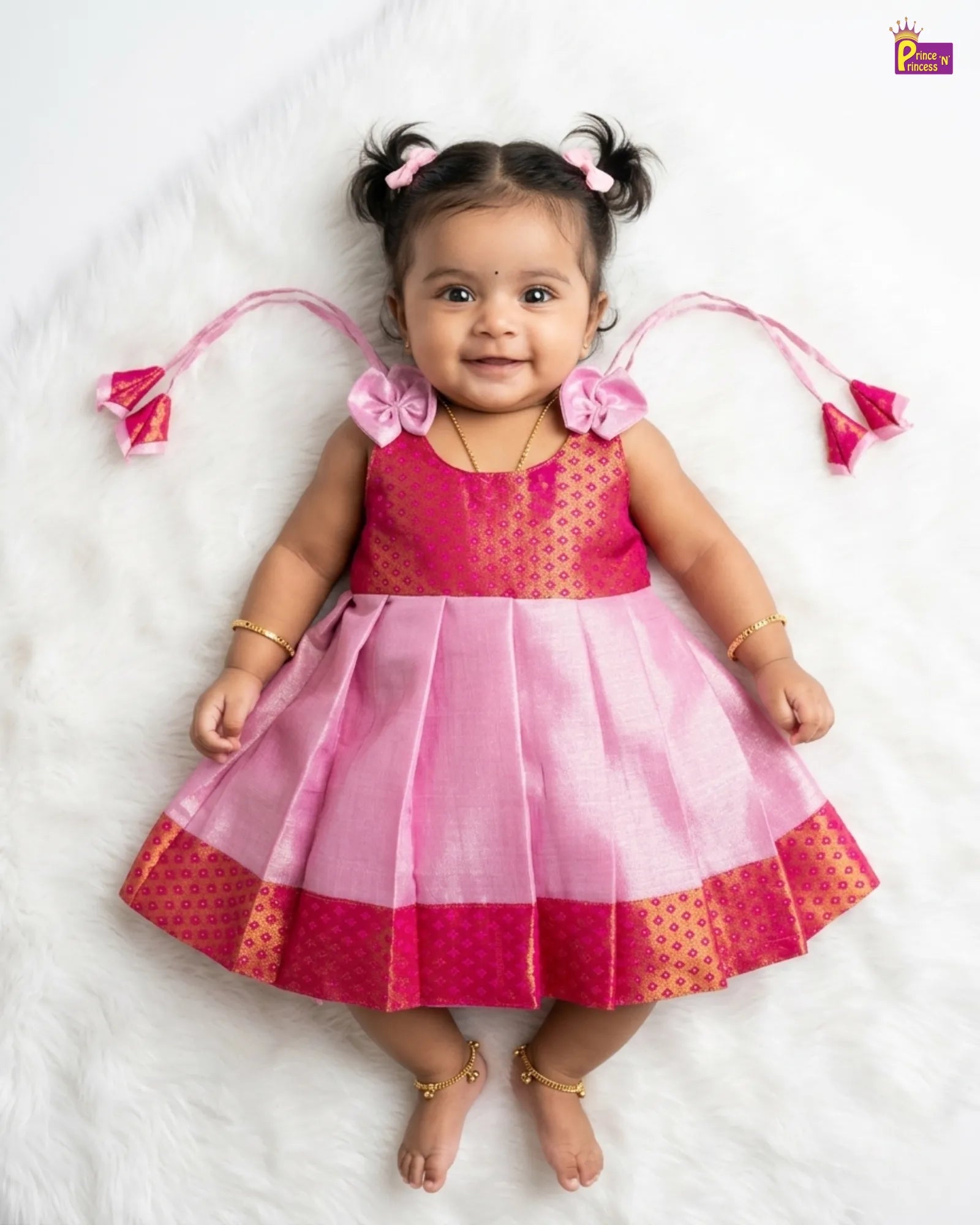 Baby wearing a pink and red dress with decorative elements on a white background