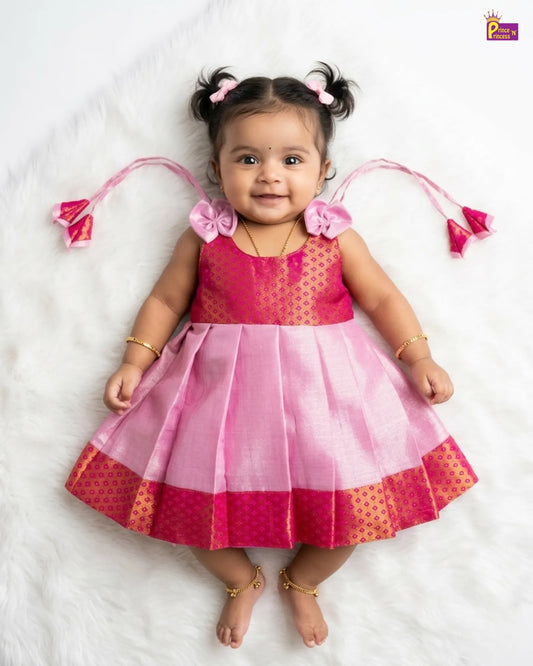 Baby wearing a pink and red dress with decorative elements on a white background