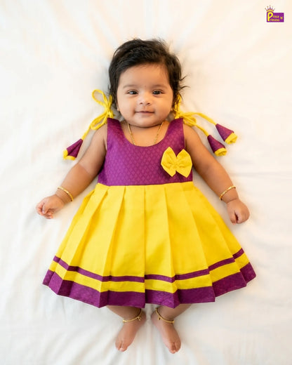 Baby wearing a yellow and purple dress with a bow on a white background