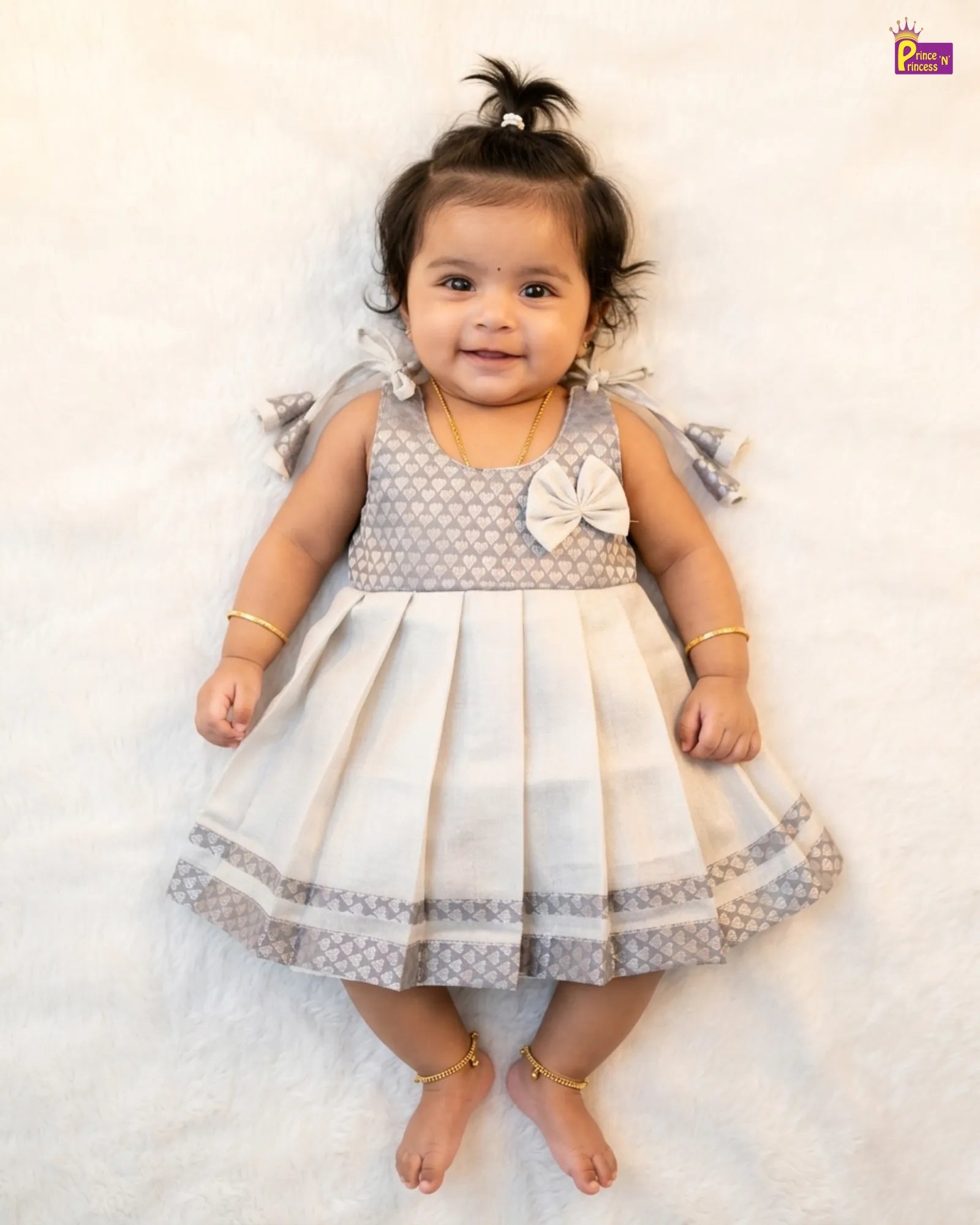 Baby wearing a gray and white dress with a bow on a white background