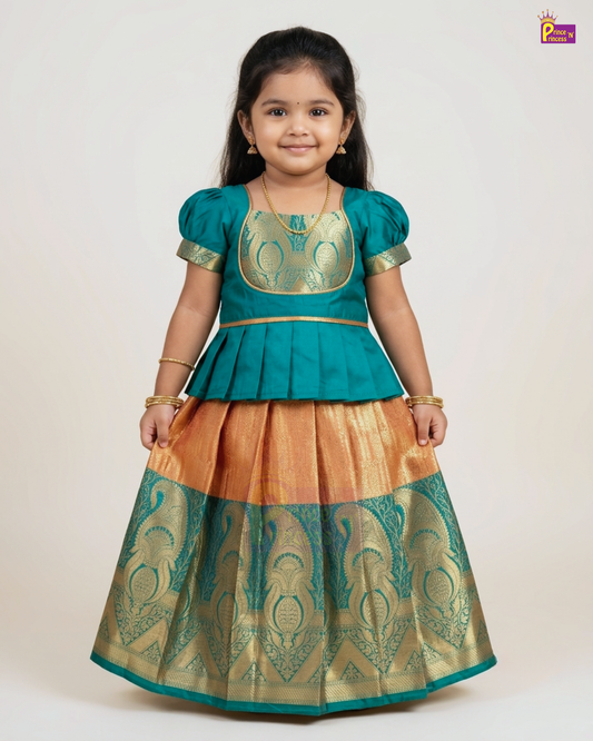 A young girl modeling a traditional Indian ethnic outfit consisting of a teal blue peplum top with gold embroidery and a matching flared skirt in gold and teal with woven patterns, set against a plain light background.