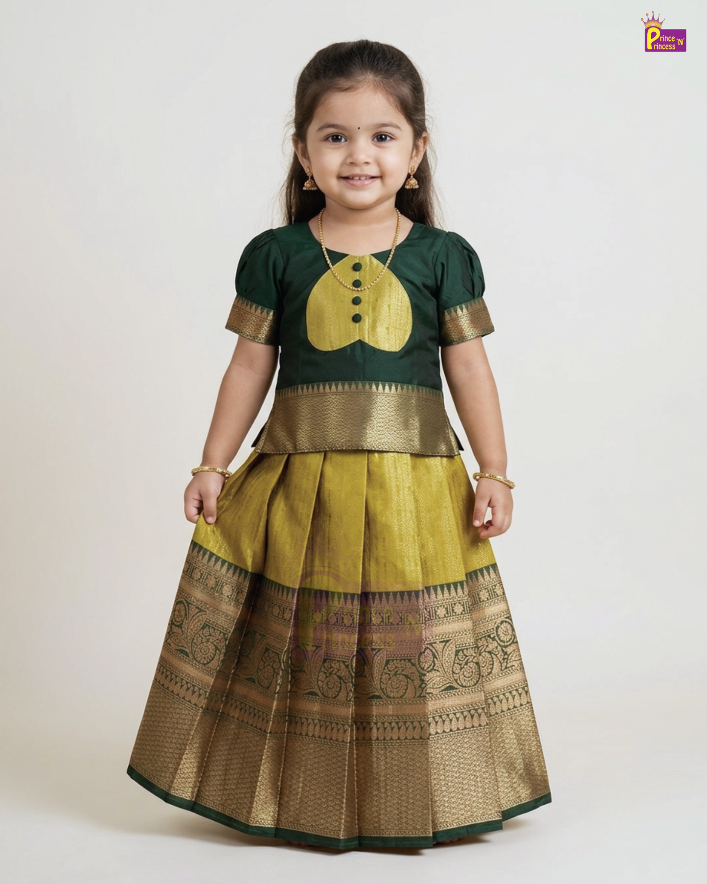 A young girl modeling a traditional Indian ethnic dress consisting of a dark green kurta with a gold yoke and a pleated gold skirt with a wide gold zari border, set against a plain light gray background.