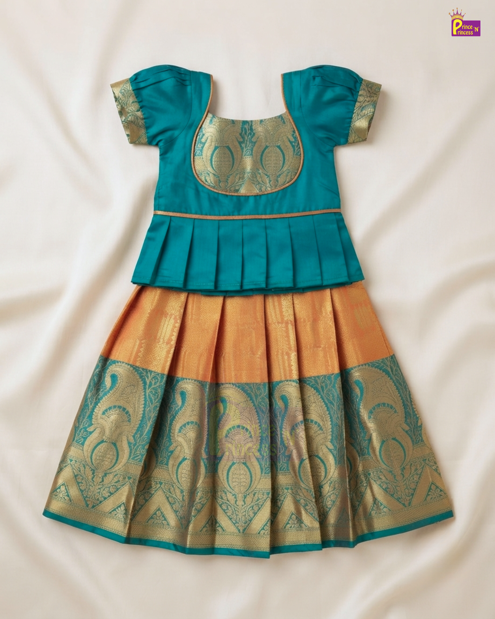 A traditional Indian toddler girl's dress featuring a teal blue peplum top with gold embroidery and a pleated skirt in mustard yellow and teal with gold zari patterns, laid flat on a cream fabric background.