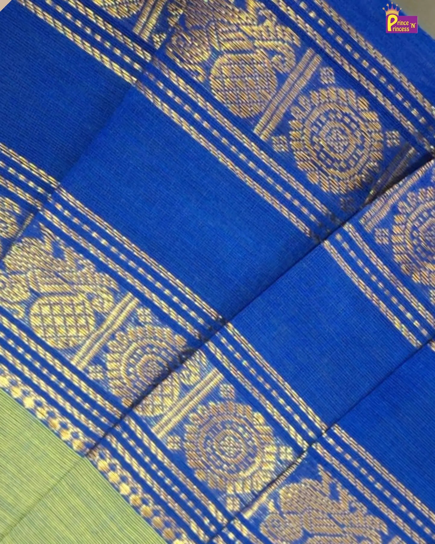 A close-up of a royal blue silk saree with intricate gold zari woven patterns and borders, showing a hint of a light green body in the bottom left corner.