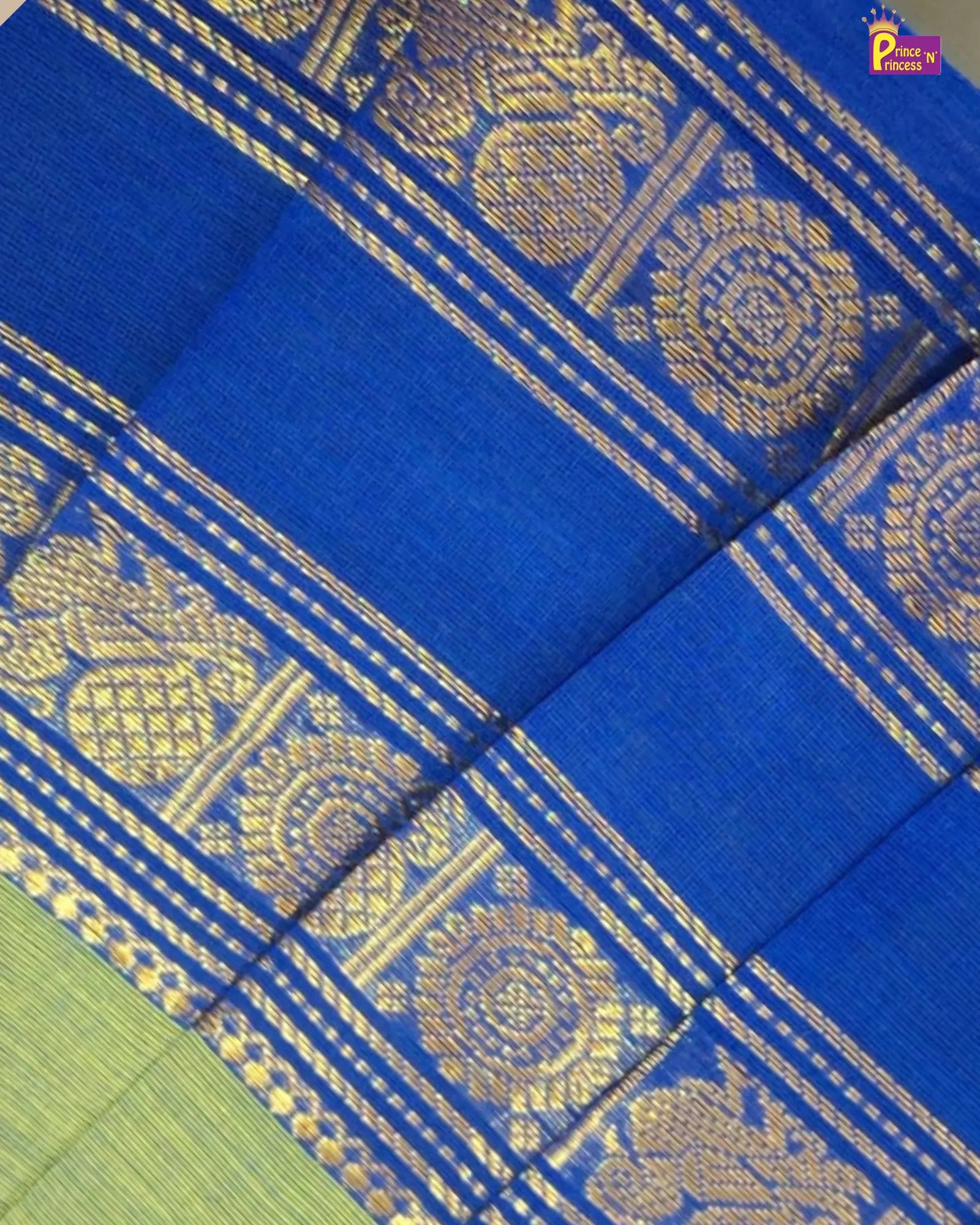 A close-up of a royal blue silk saree with intricate gold zari woven patterns and borders, showing a hint of a light green body in the bottom left corner.