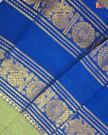 A close-up of a royal blue silk saree with intricate gold zari woven patterns and borders, showing a hint of a light green body in the bottom left corner.