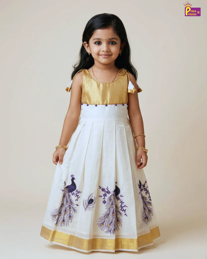Young girl wearing a white dress with peacock designs and gold accents on a plain background