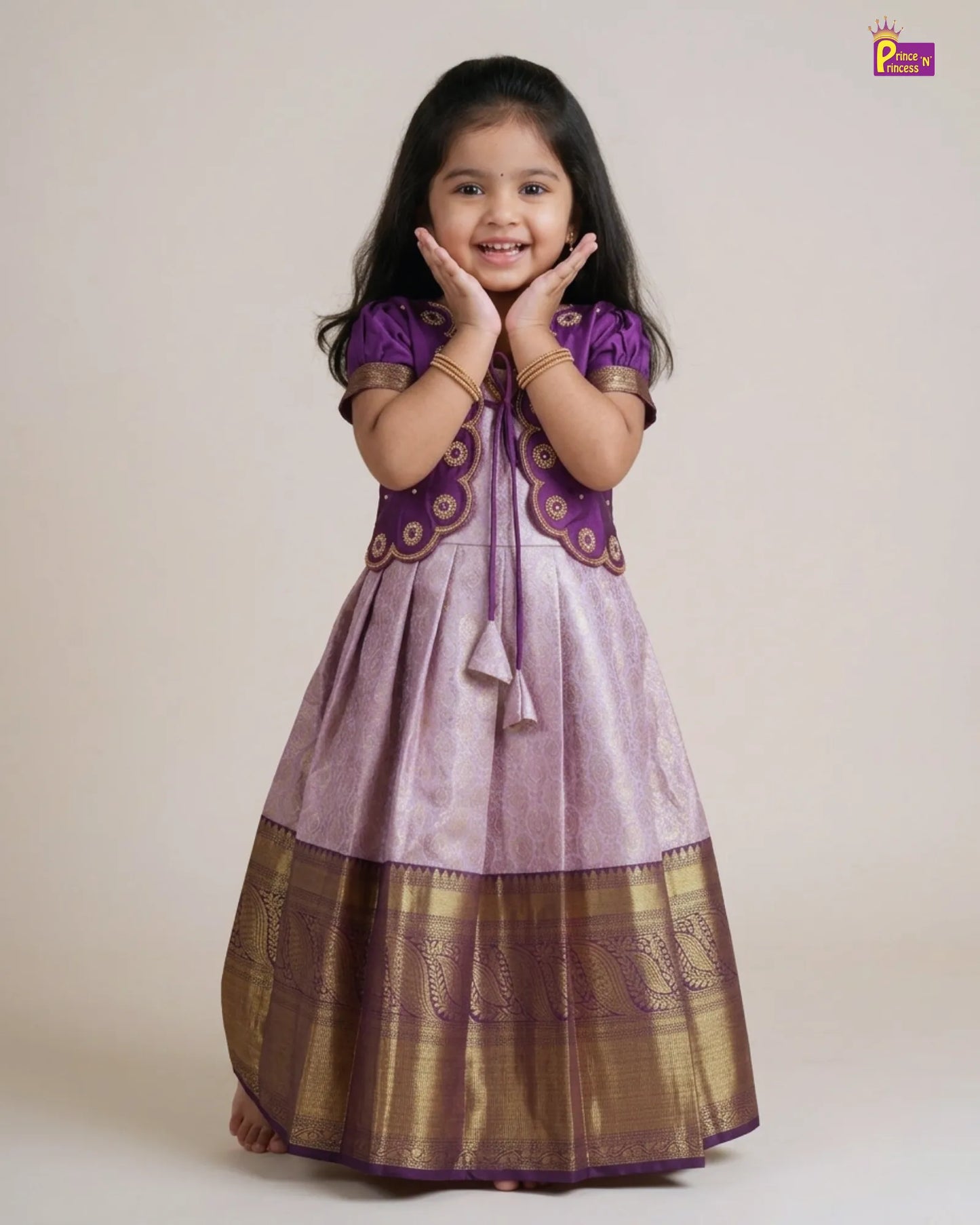 A young girl modeling a traditional Indian salwar kameez dress. The dress features a lavender-purple body with a wide metallic gold border at the hem, a matching purple embroidered yoke, and purple sleeves.
