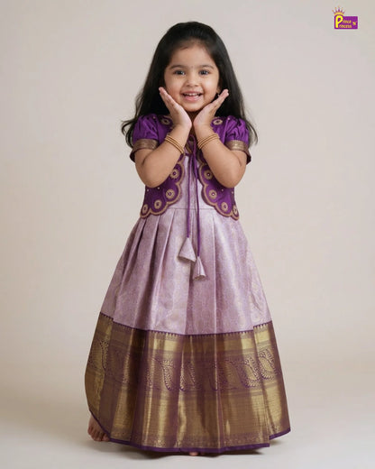 A young girl modeling a traditional Indian salwar kameez dress. The dress features a lavender-purple body with a wide metallic gold border at the hem, a matching purple embroidered yoke, and purple sleeves.