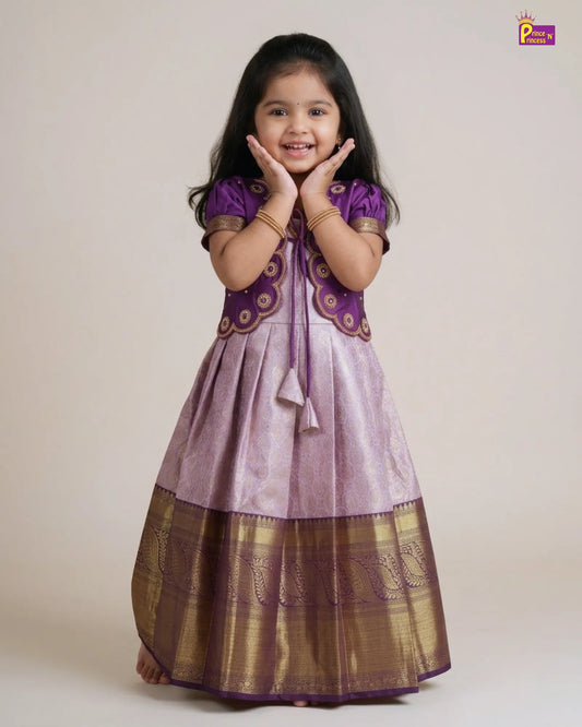 A young girl modeling a traditional Indian salwar kameez dress. The dress features a lavender-purple body with a wide metallic gold border at the hem, a matching purple embroidered yoke, and purple sleeves.