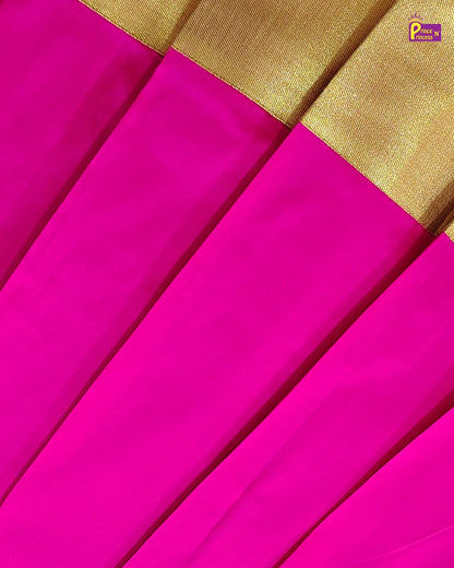 A close-up of a bright pink fabric, likely a sari, with pleated folds and a wide gold border.