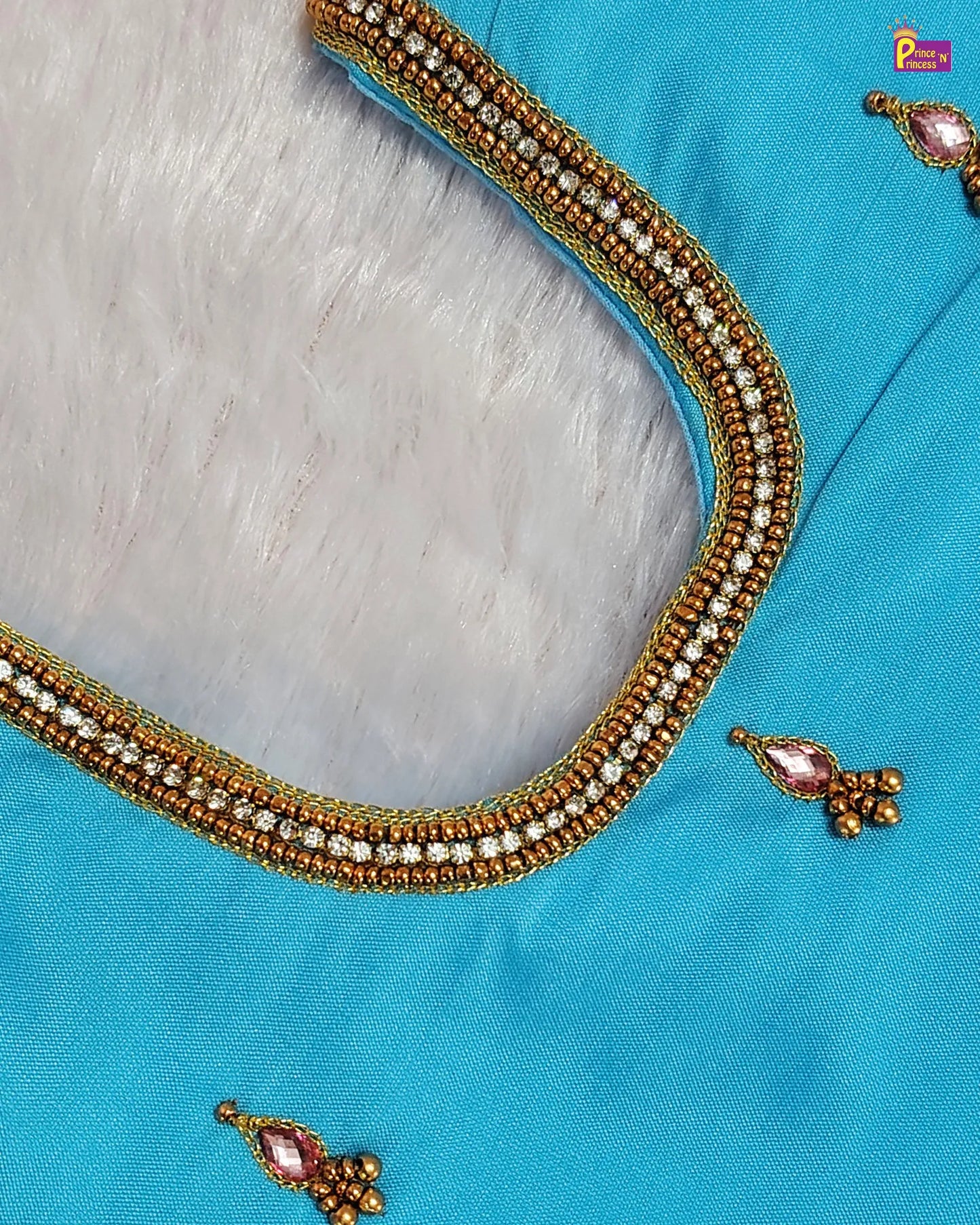 Close-up of a blue fabric with gold and pearl embroidery on a gray background