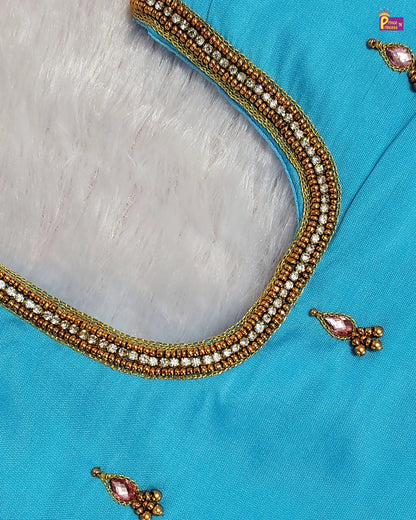 Close-up of a blue fabric with gold and pearl embroidery on a gray background