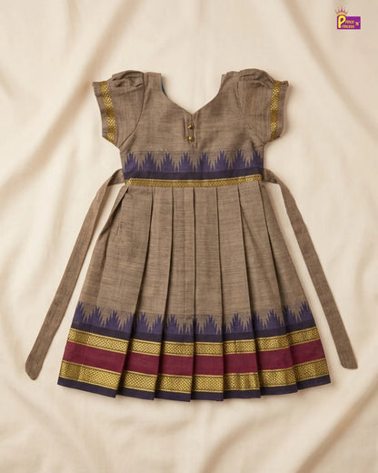 A traditional Indian girl's dress in brown fabric with a blue and gold patterned waistband and hem, laid flat on a cream-colored fabric background.