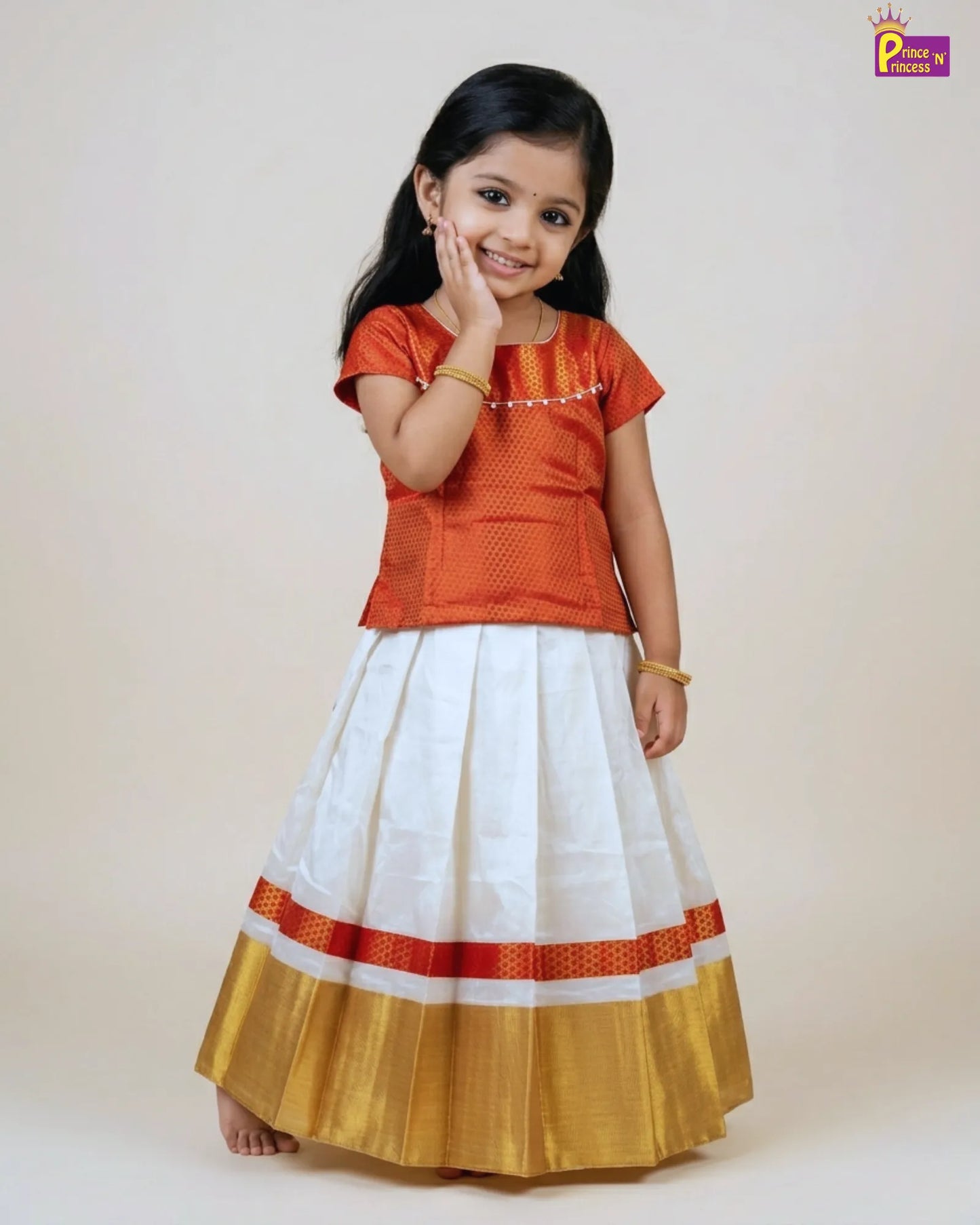 Young girl wearing an orange top and white skirt with red and gold accents on a plain background