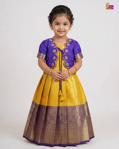 A young girl modeling a traditional Indian ethnic outfit consisting of a yellow and purple kurta with gold zari embroidery, set against a plain light gray background.