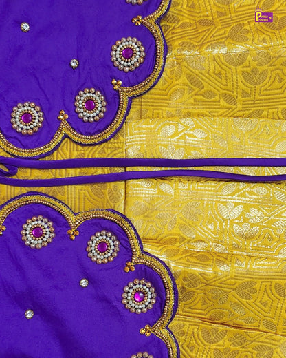 A close-up of a purple and yellow fabric textile, likely a saree or scarf, featuring a richly patterned yellow body with metallic gold motifs and matching purple borders decorated with scalloped edges, gold embroidery, and pink gemstone accents.