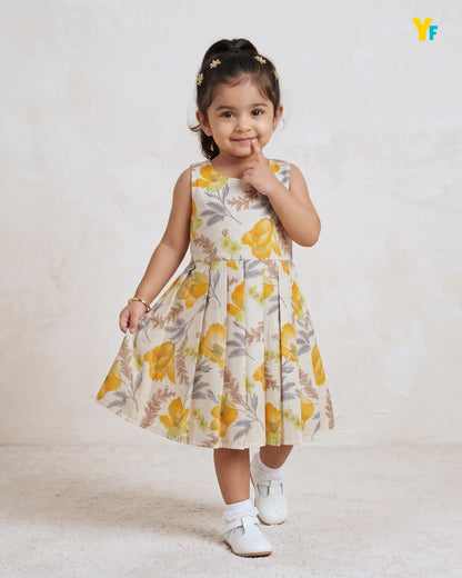 A young girl with her hair in a high ponytail wearing a sleeveless yellow floral dress, white socks, and white shoes, posing against a textured beige wall. A yellow and blue 'Yf' logo is visible in the top right corner.