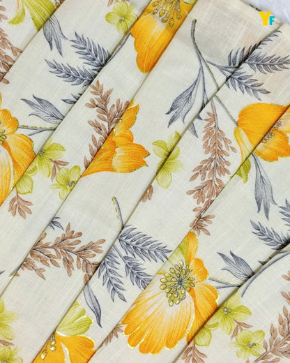 A close-up of a folded fabric or textile with a floral print. The base is a warm off-white/cream color, decorated with large yellow-orange flowers, green leaves, and brown and gray botanical details.