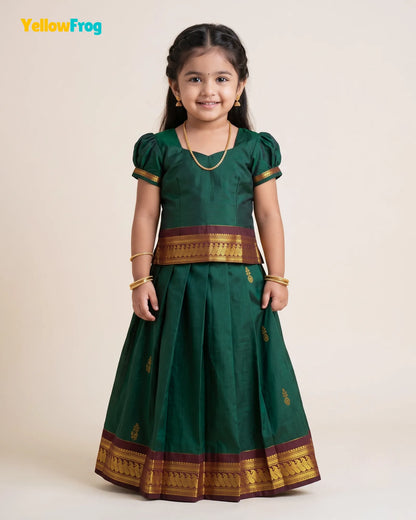 A young girl modeling a dark green traditional Indian dress with gold and maroon borders, standing against a plain beige background. The YellowFrog logo is visible in the top left corner.