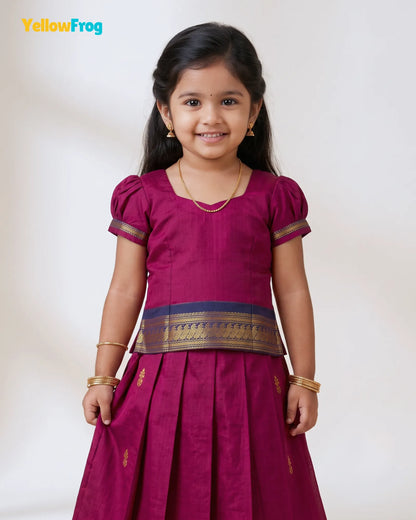 A young girl modeling a traditional Indian salwar kameez outfit in magenta with gold and navy accents, standing against a plain off-white background. The YellowFrog brand logo is visible in the top left corner.