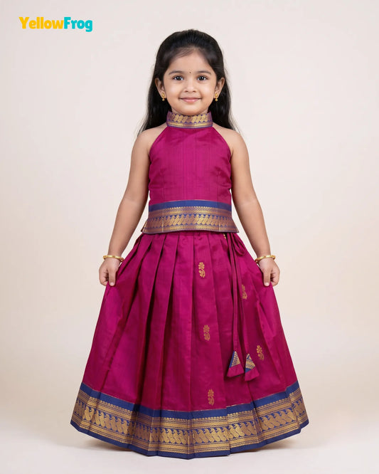 A young girl modeling a magenta pink traditional Indian dress with gold and blue zari borders, standing against a plain beige background. The YellowFrog logo is visible in the top left corner.