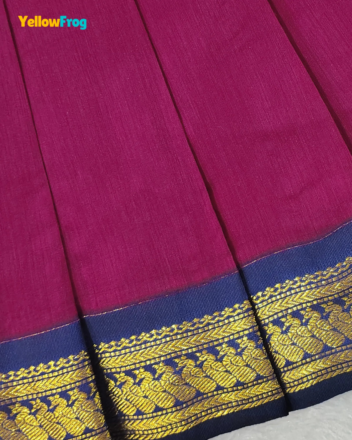 A close-up of a magenta-pink fabric with a wide navy blue border featuring intricate gold woven patterns, with a YellowFrog logo in the top left corner.