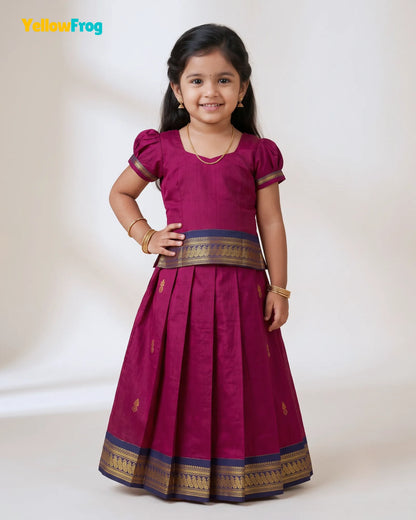 A young girl modeling a magenta traditional Indian dress with gold and navy borders, standing against a plain off-white studio background. The YellowFrog logo is visible in the top left corner.